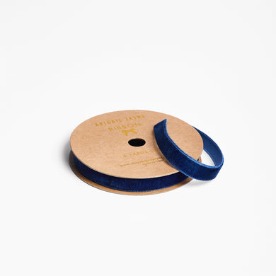 Spool of navy blue velvet ribbon on a cardboard reel with a white background