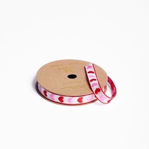 Spool of woven ribbon with pink and red heart pattern on a white background
