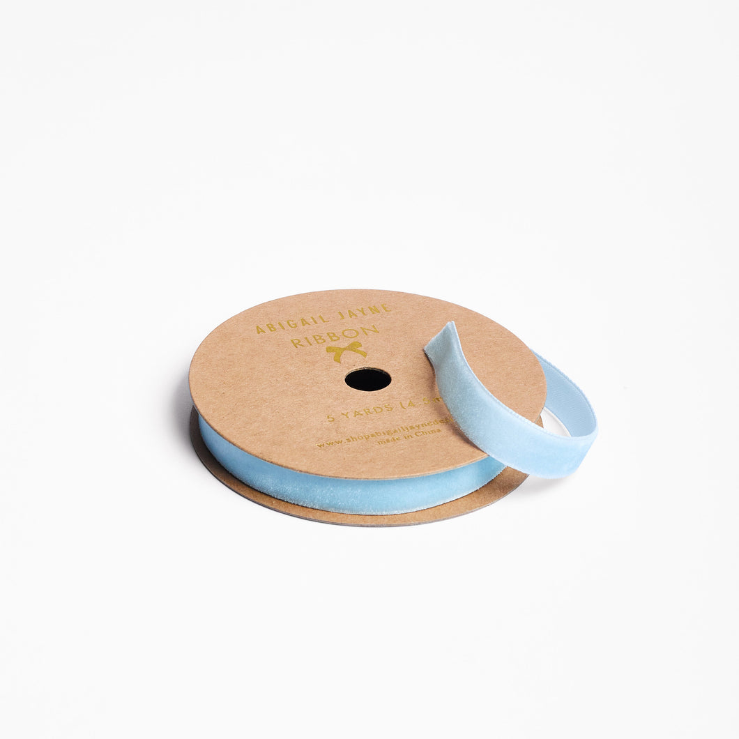 Spool of light blue velvet ribbon on a cardboard reel with a visible brand logo.